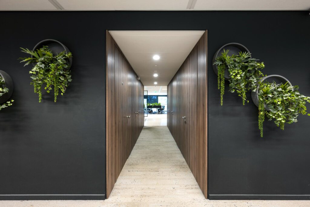 Modern office hallway on Gustav Mahlerlaan with dark walls, wooden panels, and circular wall planters with cascading greenery.